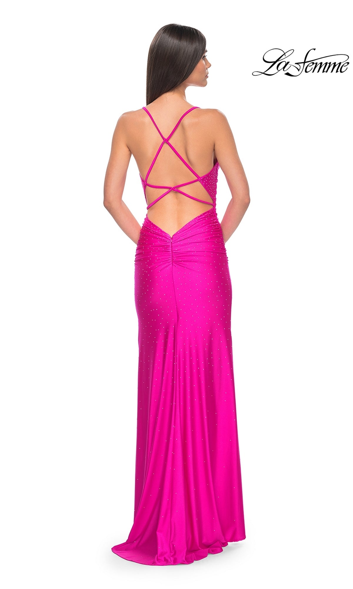 A woman in the La Femme Backless Long Beaded Prom Dress 32317, featuring bright pink fabric, rhinestone details, and a strappy open back, stands facing away.